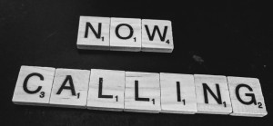 Scrabble tiles on a black background, spelling out "Now Calling"